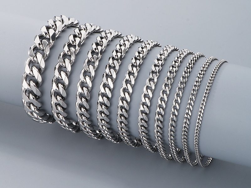 A collection of silver-plated stainless steel chain bracelets displayed on a cylindrical stand. The bracelets vary in thickness and design, showcasing a sleek, polished finish for a modern and stylish look.