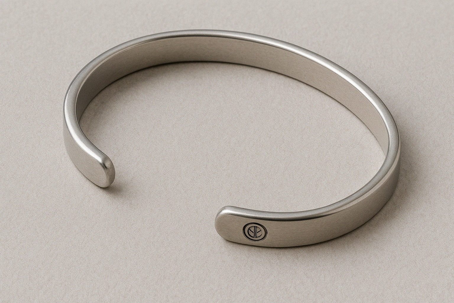 Close-up of a minimalist stainless steel cuff bracelet with an open-ended design and engraved logo on one tip.