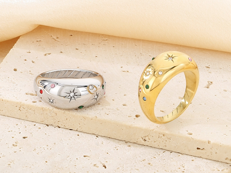 Silver and gold dome rings featuring engraved starburst patterns and multicolored gemstone accents, displayed on stone tiles