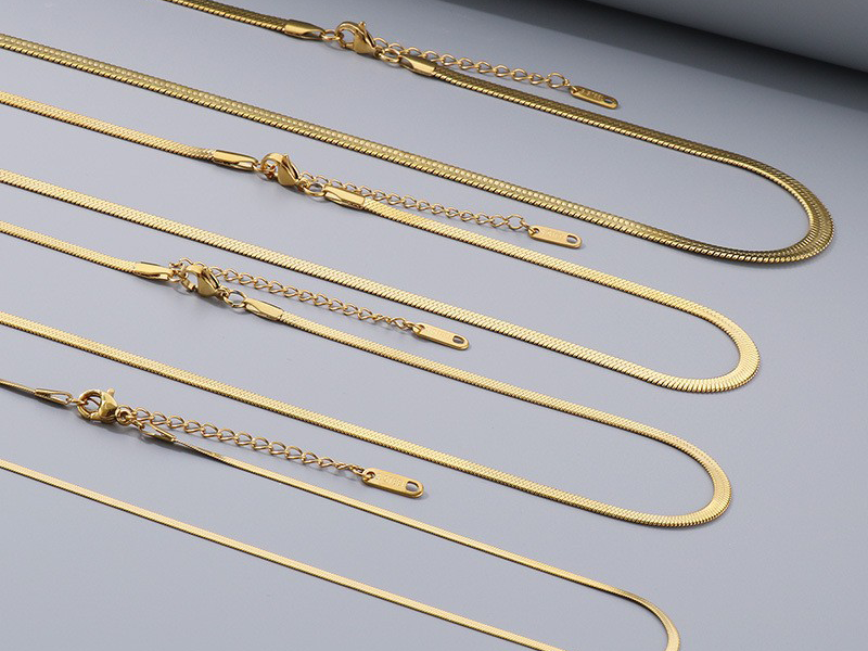 Multiple flat gold snake chain necklaces with adjustable extension clasps arranged on a gray background.