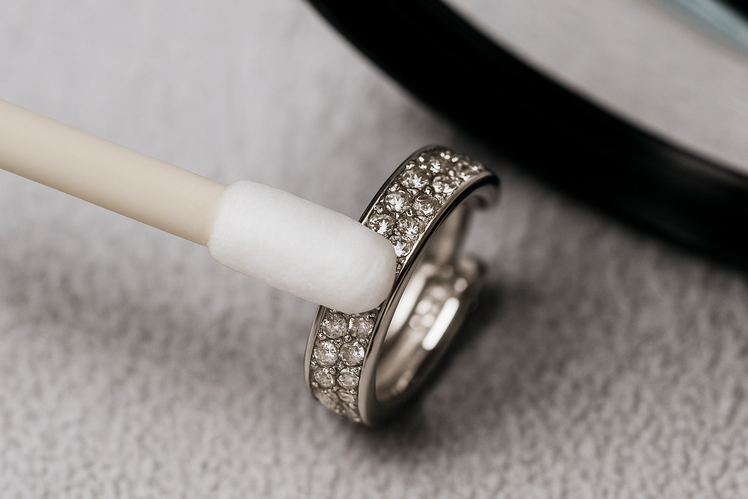Close-up of a foam swab cleaning a pavé-set diamond earring under a magnifier, illustrating a gem-safe method.