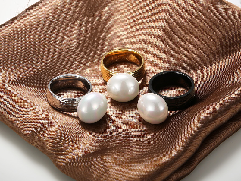 Three luxurious pearl rings in silver, gold, and black finishes displayed on brown satin fabric